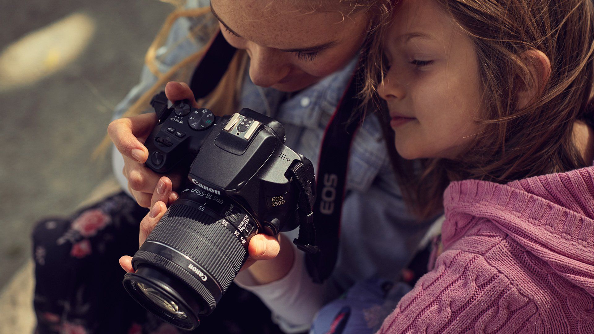A woman lifts a Canon EOS 250D to take a photo of her daughter.
